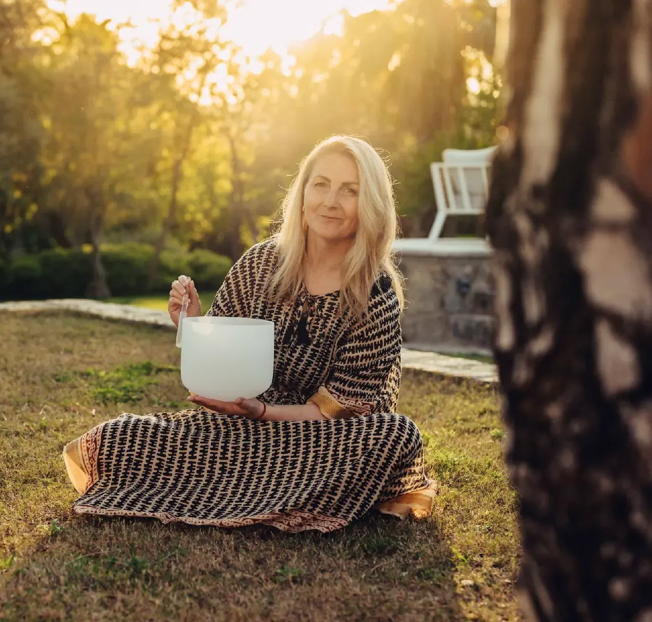 Kerstin sitzt im Abendlicht auf einer Wiese und hält eine Klangschale.