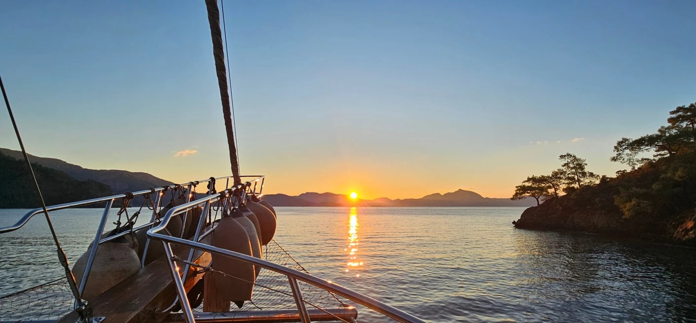 Sonnenaufgang über einer ruhigen Bucht, im Vordergrund der Bug der Larin Su mit Fendern