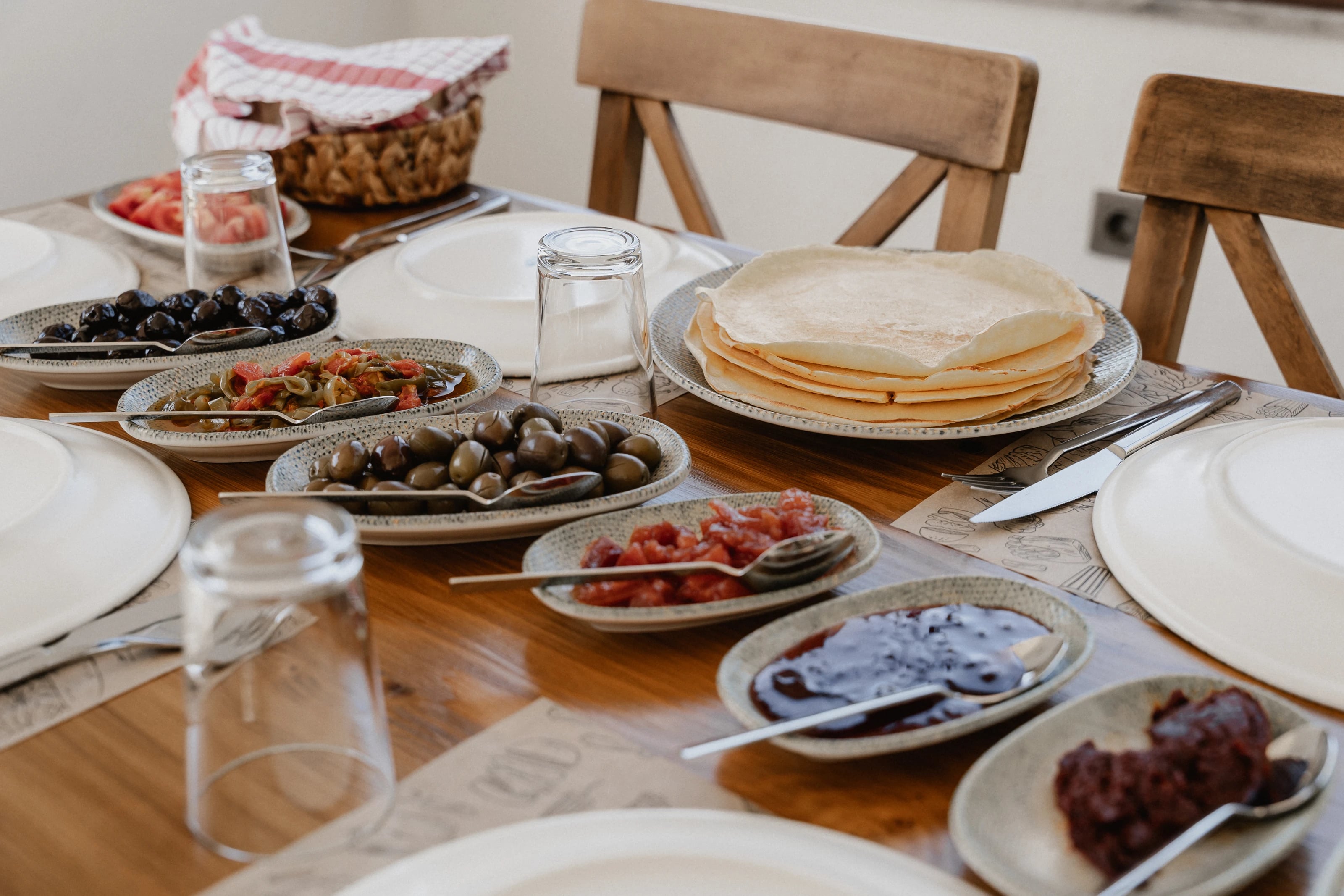 Türkisches Frühstück auf Holz: Oliven, Tomatensalat, Marmelade und ein Stapel Fladenbrot.