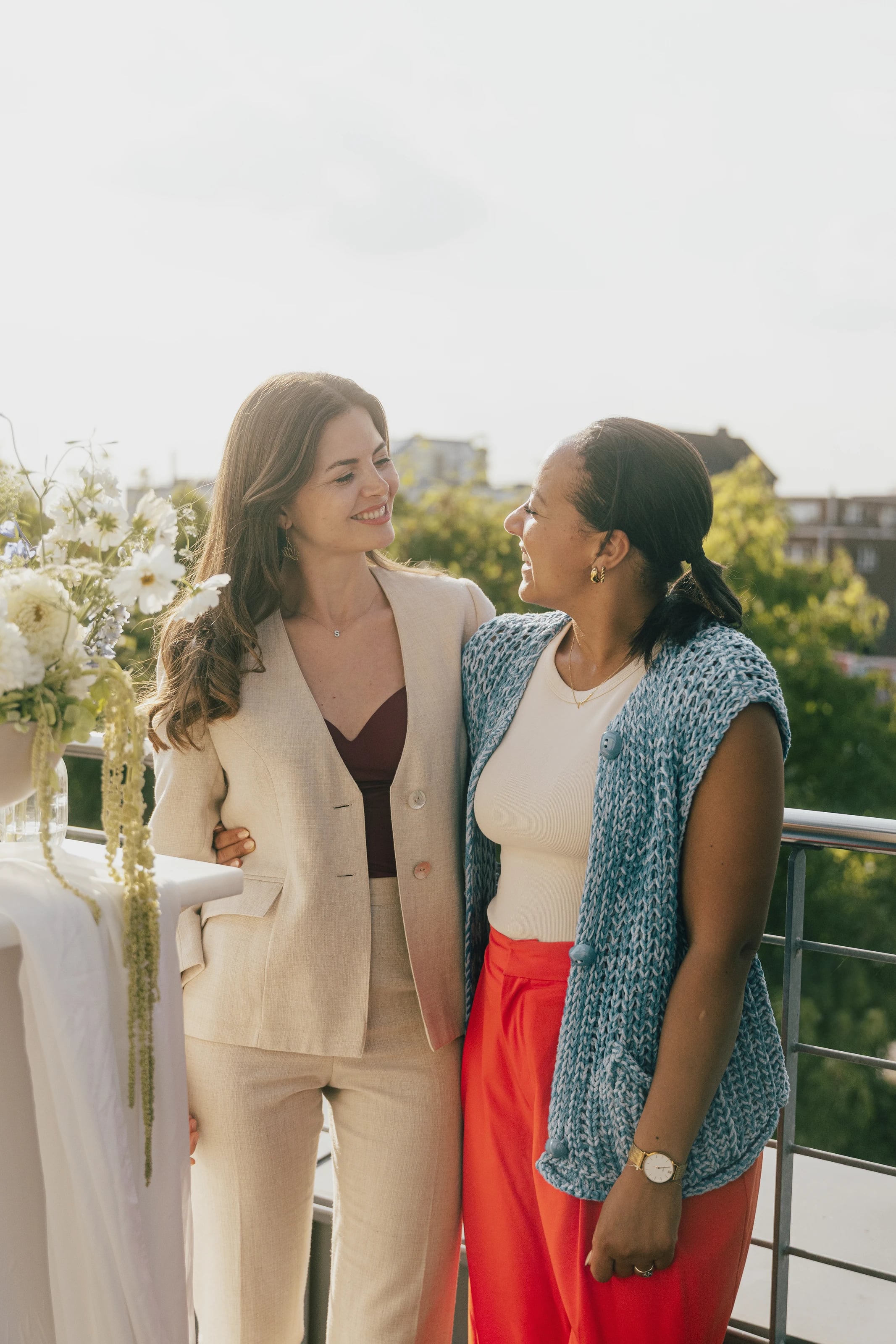Zwei Frauen umarmen sich auf einer Dachterrasse vor der Skyline.