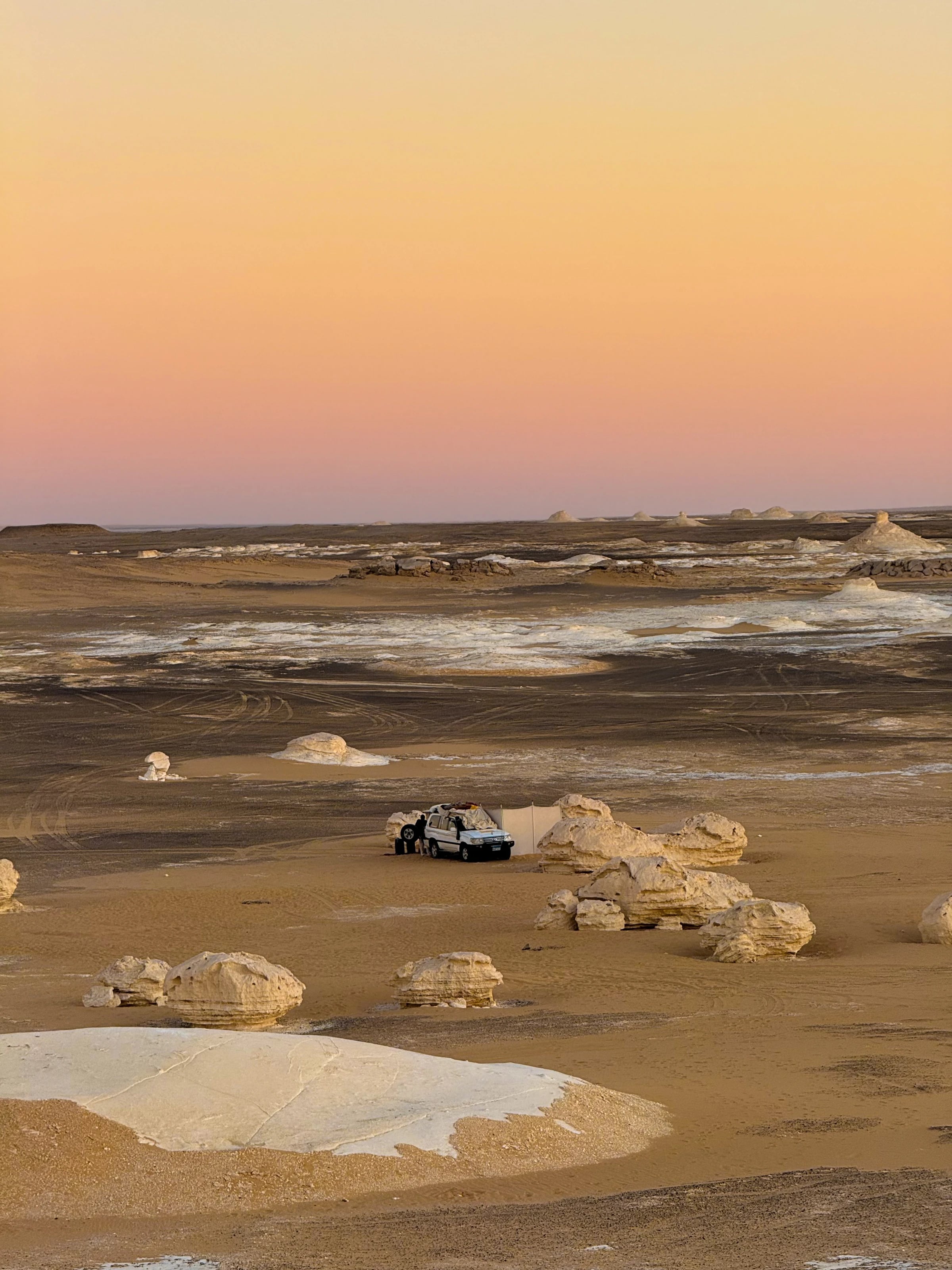 Weiter Sonnenuntergang über der Weißen Wüste mit Jeep und Zeltlager zwischen Kreidefelsen.